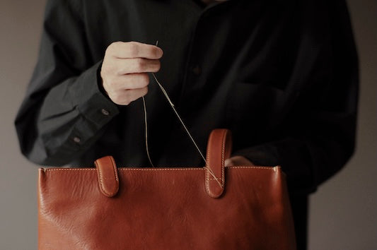 Person holding a brown leather bag with a black shirt.